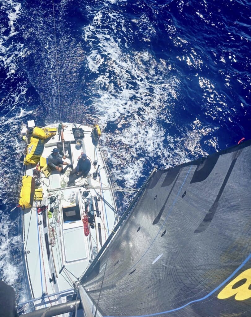 Masthead view down onto Dorado's deck and dark headsail, deep blue Pacific water astern