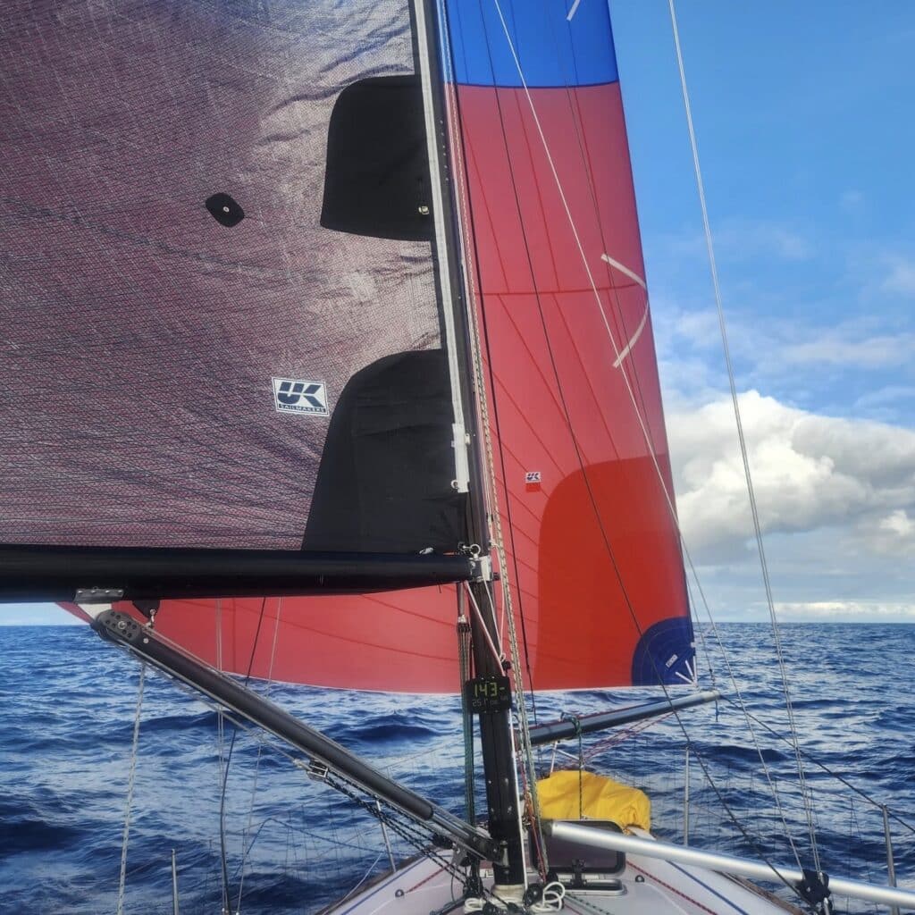 Looking up at Dorado's dark UK Sailmakers mainsail and red spinnaker on a downwind Pacific leg