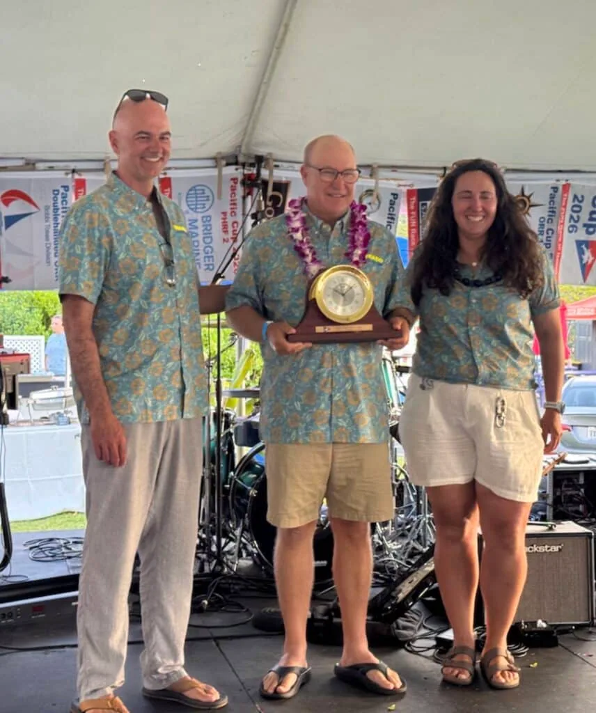 Three Dorado crew members accept a Pacific Cup 2026 trophy clock on stage in aloha shirts