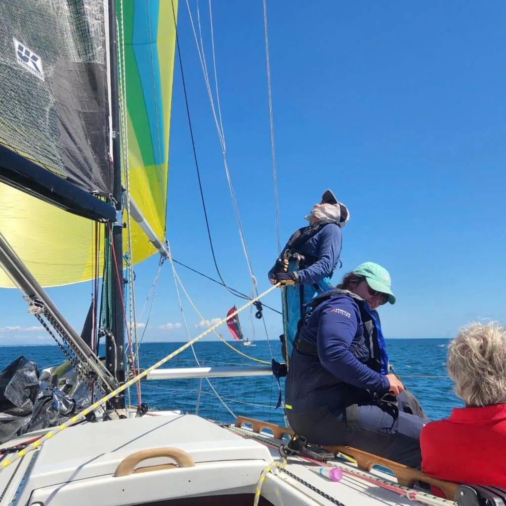 Crew on the foredeck of a racing yacht under a yellow-green spinnaker, one climbing on the boom