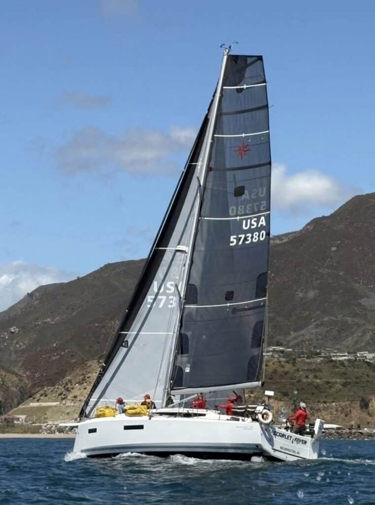 Scarlet Fever, USA 57380, sailing upwind under grey UK Sailmakers sails below coastal hills