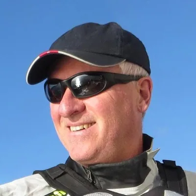 Alex Fox in a dark cap and wraparound sunglasses, smiling on the water under a clear blue sky