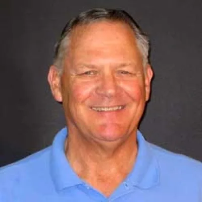 Butch Ulmer smiling in a light blue polo shirt against a dark background