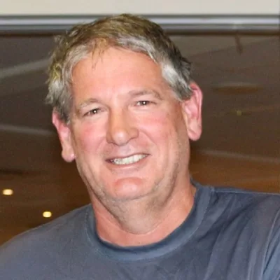 Geoff Bishop smiling in a grey T-shirt, photographed indoors with warm lighting