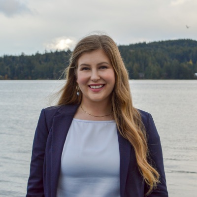 Heather Mahady in a navy blazer, smiling at a waterfront with a forested shoreline behind her