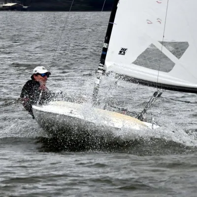 Mike Considine hiking out hard on a small dinghy in a burst of spray, UK Sailmakers logo on the mainsail