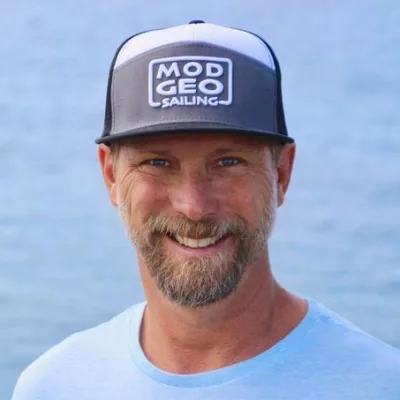 Paul Exner smiling in a Mod Geo Sailing cap and light blue T-shirt, with the sea behind him
