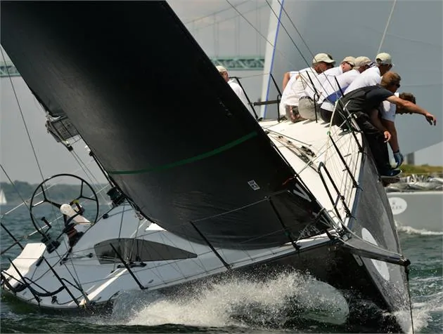 CHRISTOPHER DRAGON heeled hard upwind under a black headsail, crew stacked on the rail and spray off the bow