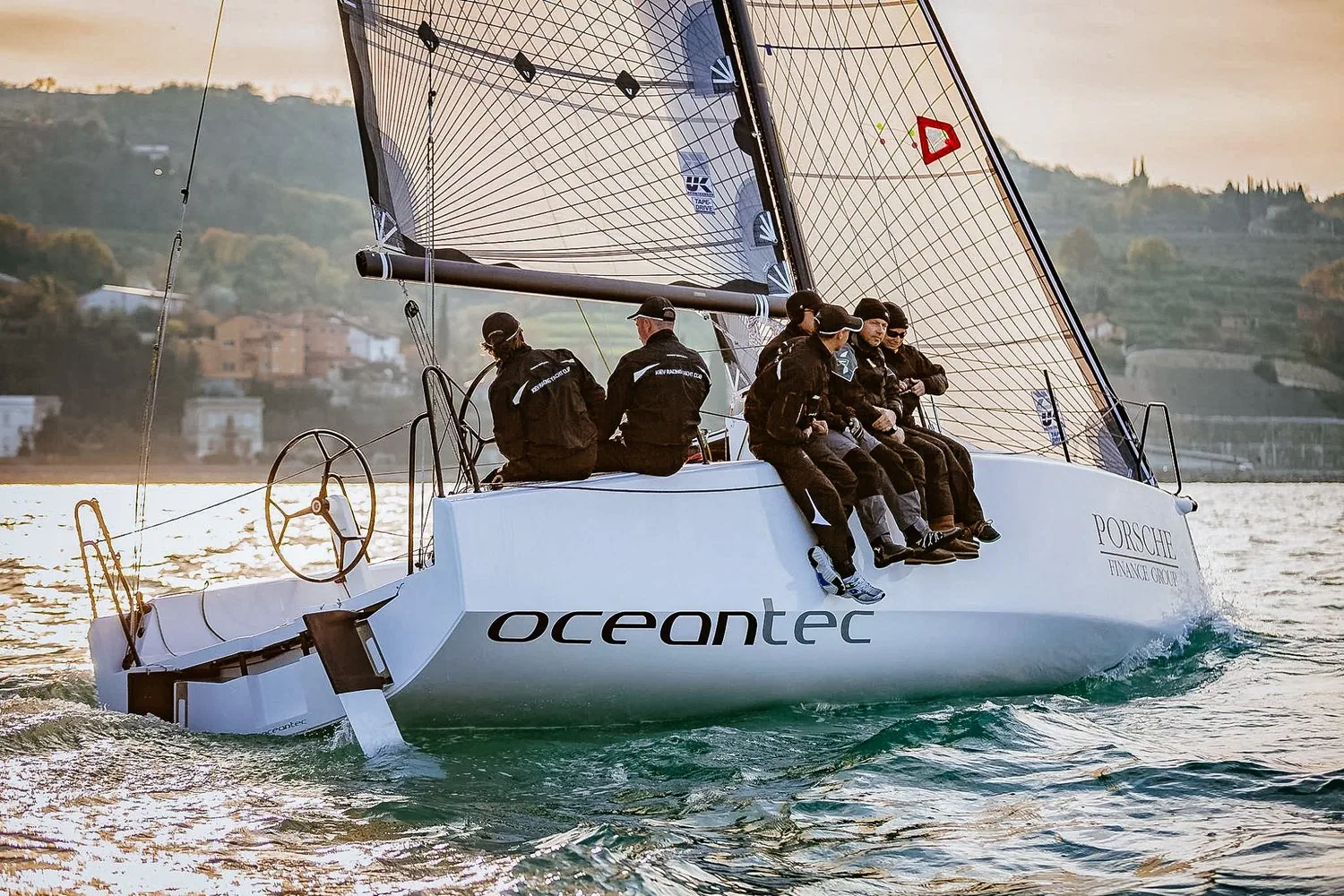 Luka 30 with 'oceantec' hull branding sailing upwind at sunset, five crew hiking on the rail
