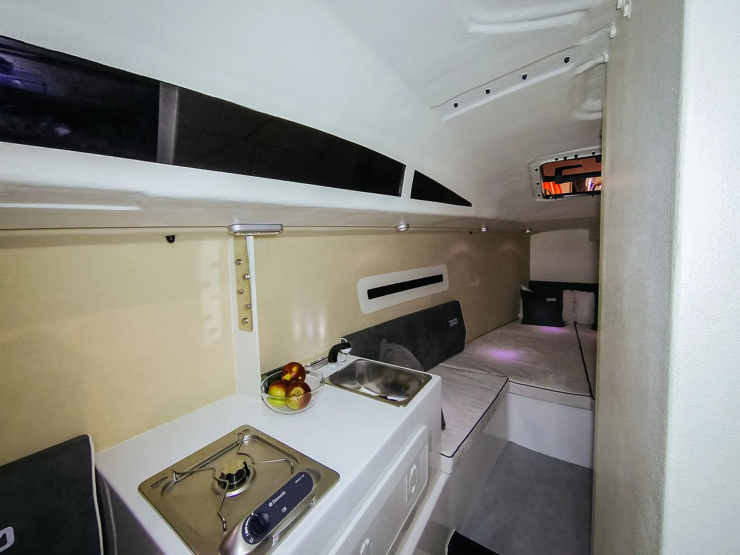 Luka 30 interior: compact galley with a two-burner stove and sink, berths and cushions further aft