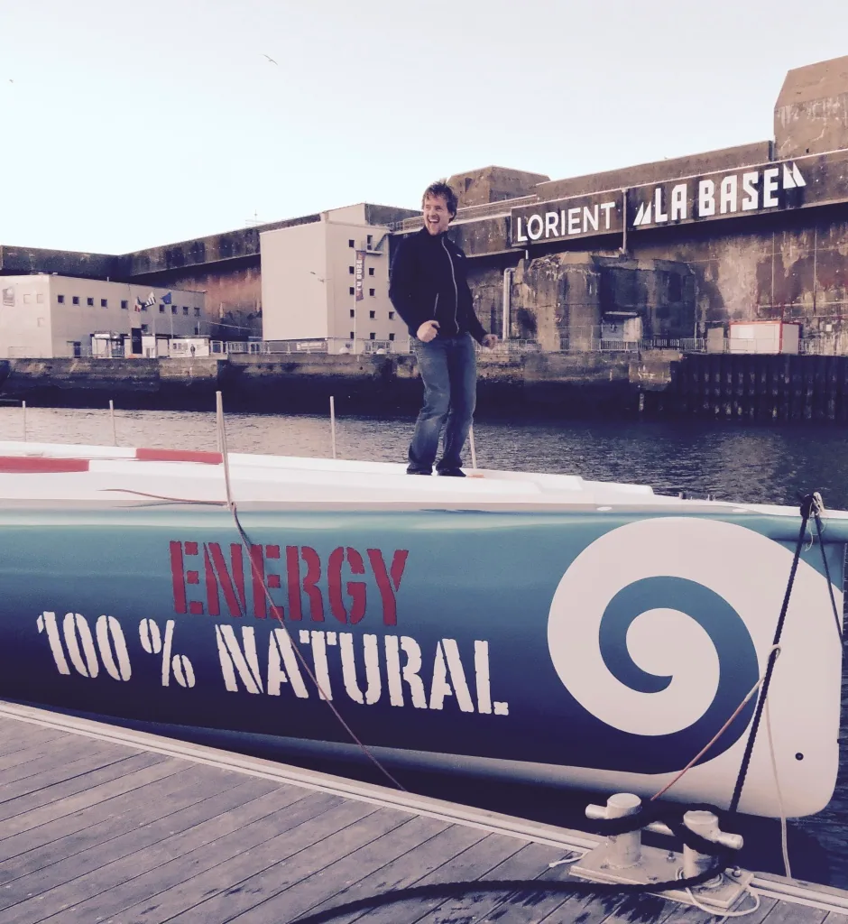Conrad Colman standing on deck at Lorient La Base, 'Energy 100% Natural' painted on the hull