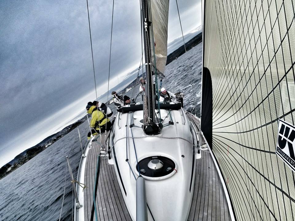 Looking aft from the bow under a grey UK Sailmakers genoa, crew in foul-weather gear beneath dark clouds