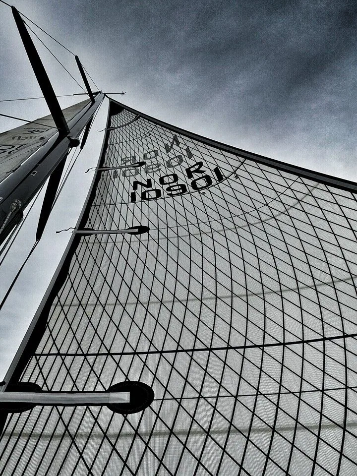 Looking up a grey laminate mainsail with a black diagonal grid and sail number NOR 10901 against storm clouds