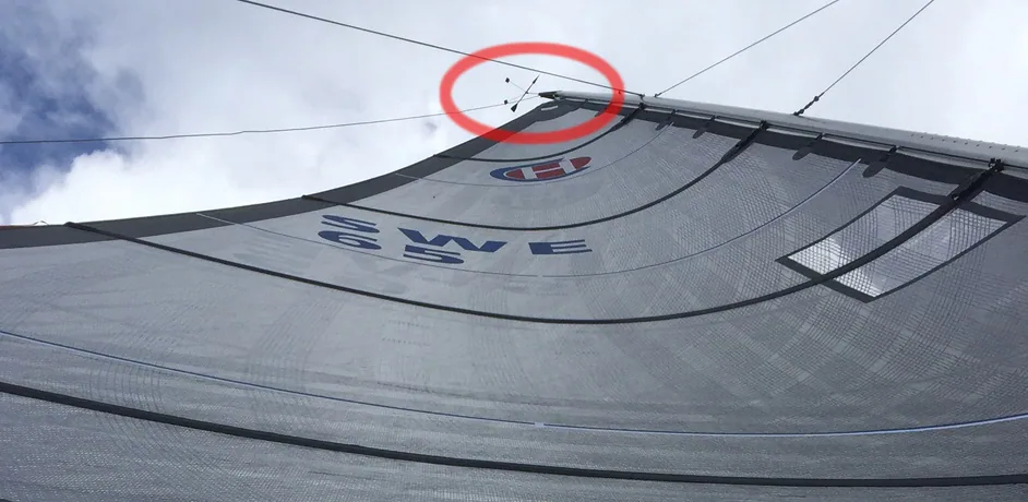Grey mainsail SWE 63 seen from below, a red circle highlighting the masthead wind indicator
