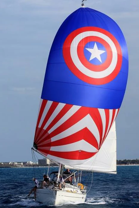 Yacht running under a Captain America-themed spinnaker: blue with a star shield and red-and-white sunburst stripes
