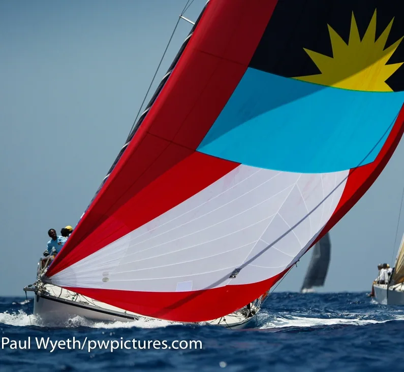 Antigua-flag spinnaker in red, blue, black and white with a yellow sun filling downwind at Antigua Sailing Week