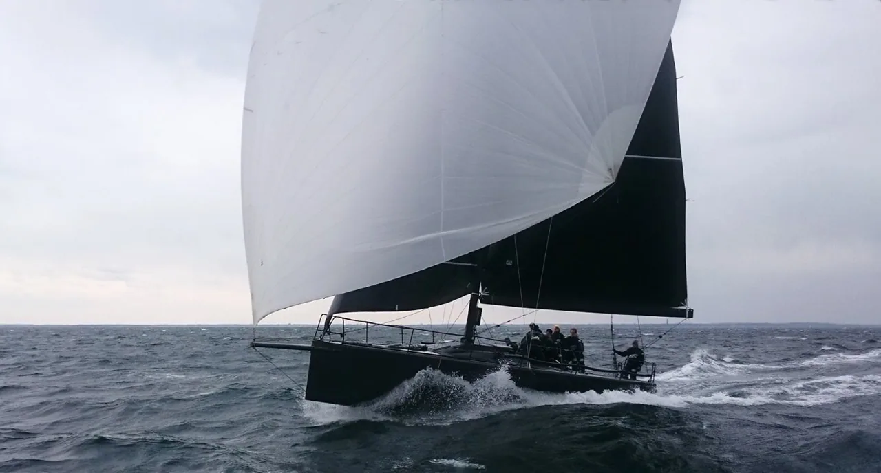 GP 42 SILVA NEO planing downwind under a white gennaker and black mainsail, crew crouched aft in grey conditions