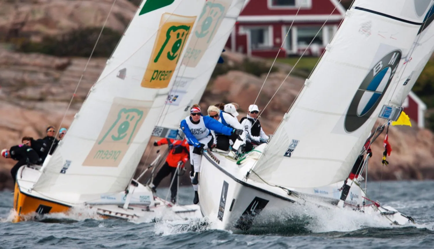 Stephanie Roble's keelboat leading Anna Östling's in a match-race final, crews hiking, red house on the rocky shore