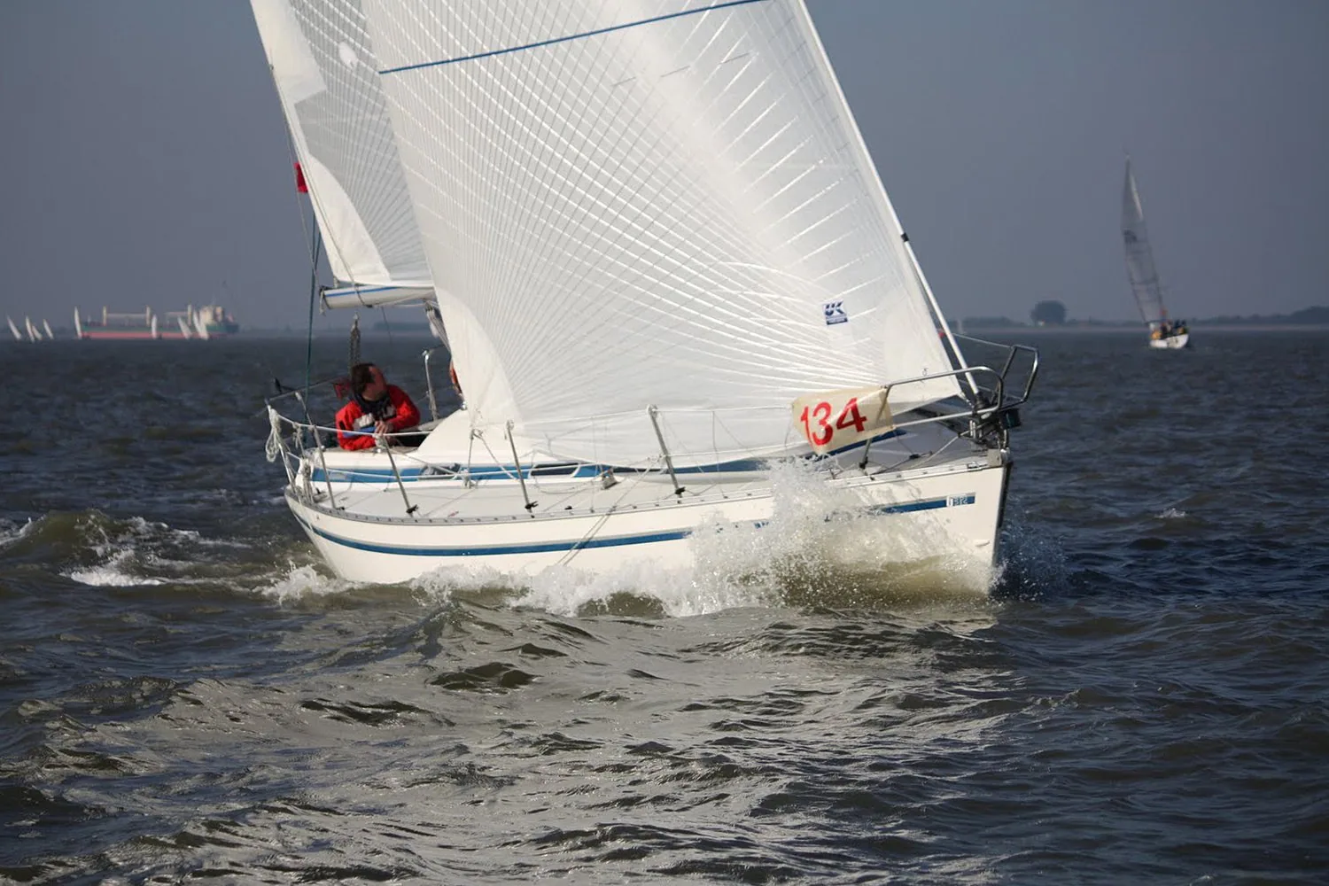 White cruiser-racer, sail number 134, heeling upwind under white mainsail and genoa with two crew in red jackets