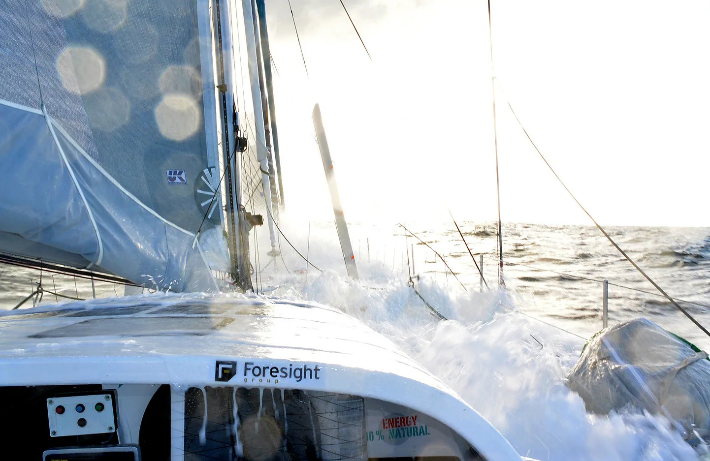 Spray sweeping the deck of Conrad Colman's IMOCA 60 Foresight Natural Energy, seen from the cockpit under sail