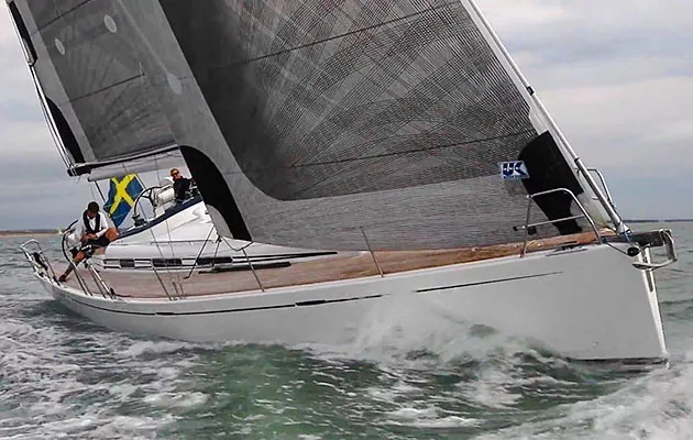 Arcona 465 heeling under black membrane mainsail and jib with a Swedish flag and two crew on the teak deck