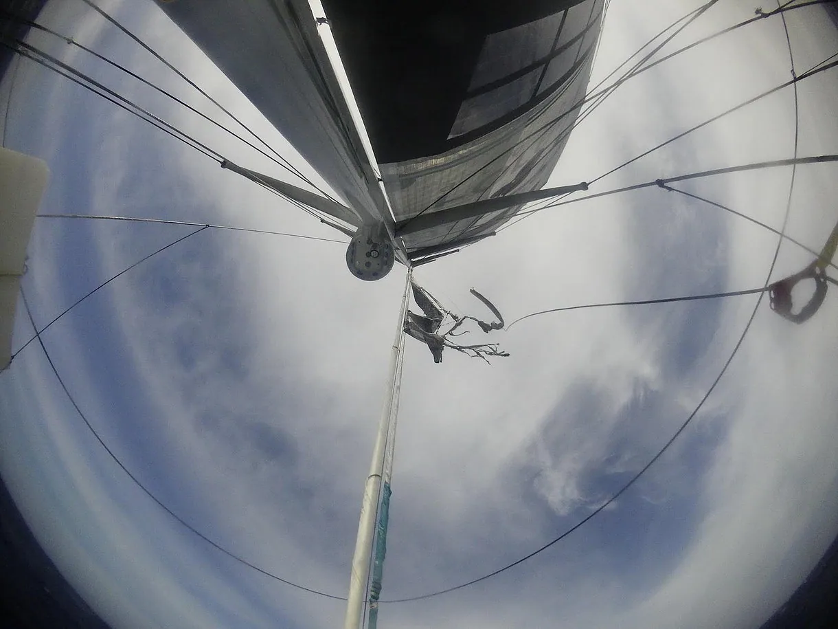 Fisheye view up the mast of Conrad Colman's IMOCA 60 with boom, spreaders and rigging against a cloudy sky