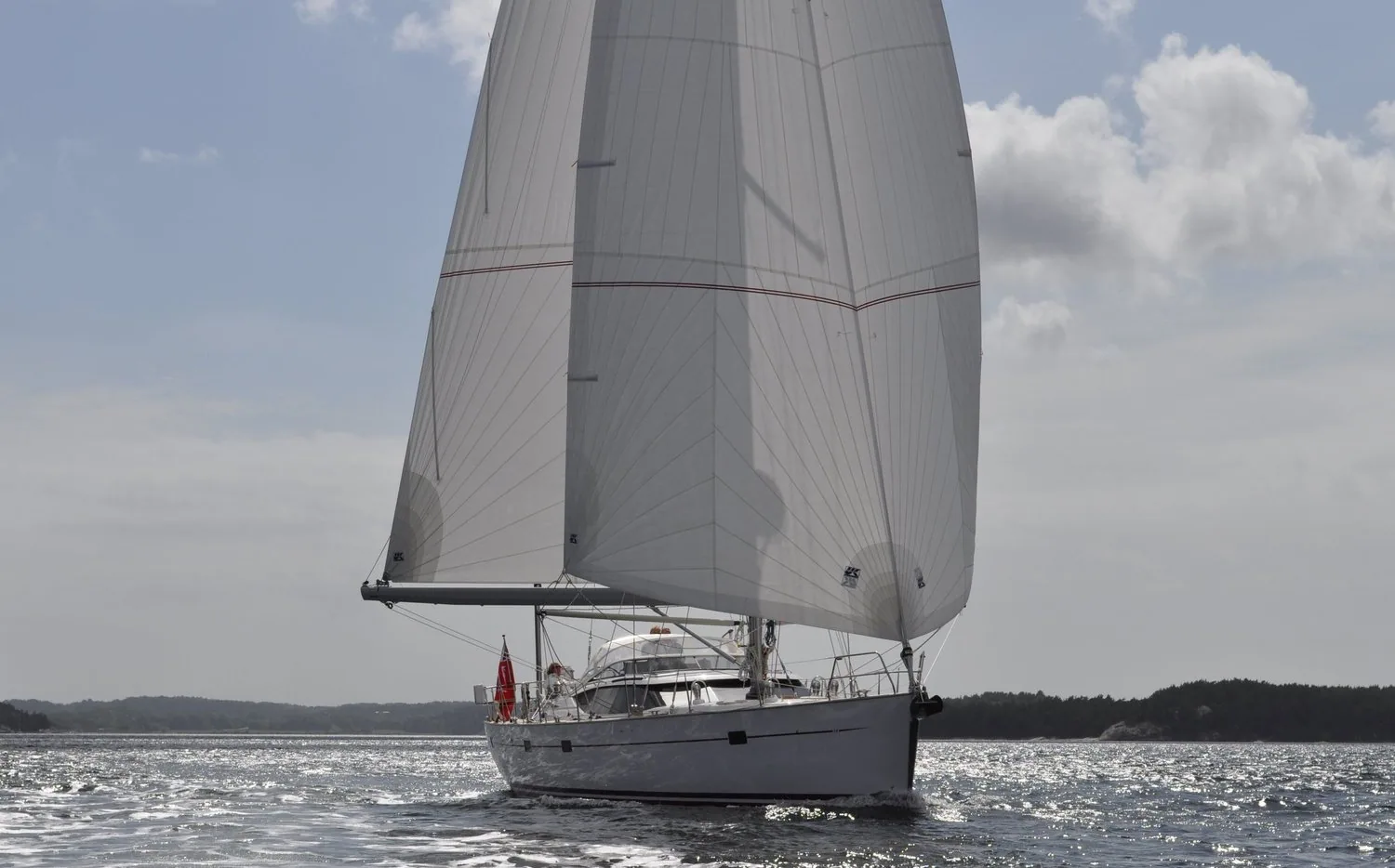White cruising yacht running downwind under twin headsails poled out either side with the mainsail furled