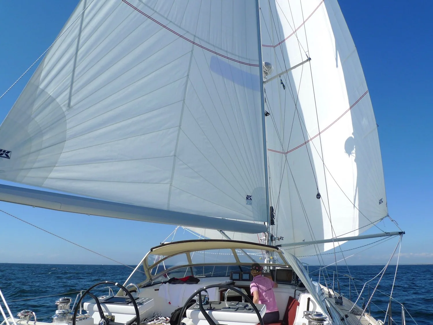 Twin white headsails set wing-and-wing seen from the cockpit of a cruising yacht under a bimini on a blue-sky day