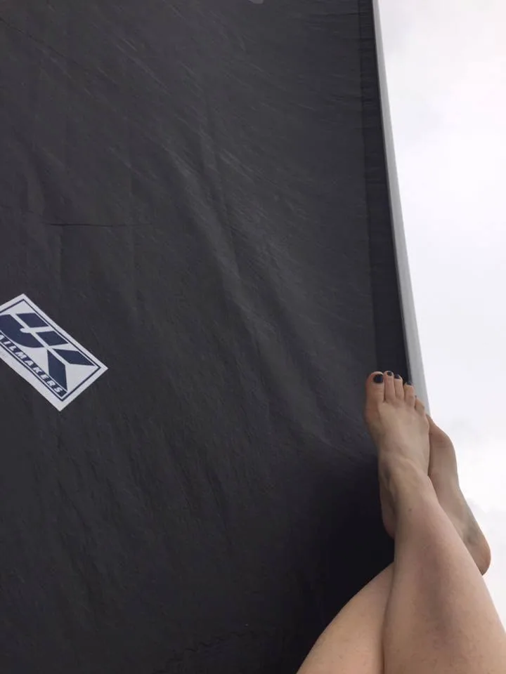 Bare feet resting on a black UK Sailmakers Titanium J/105 jib laid flat, logo visible