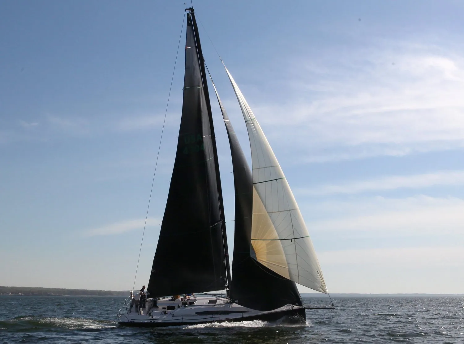 Yacht sailing with a black mainsail and a translucent flying jib set from the bowsprit in hazy sunlight
