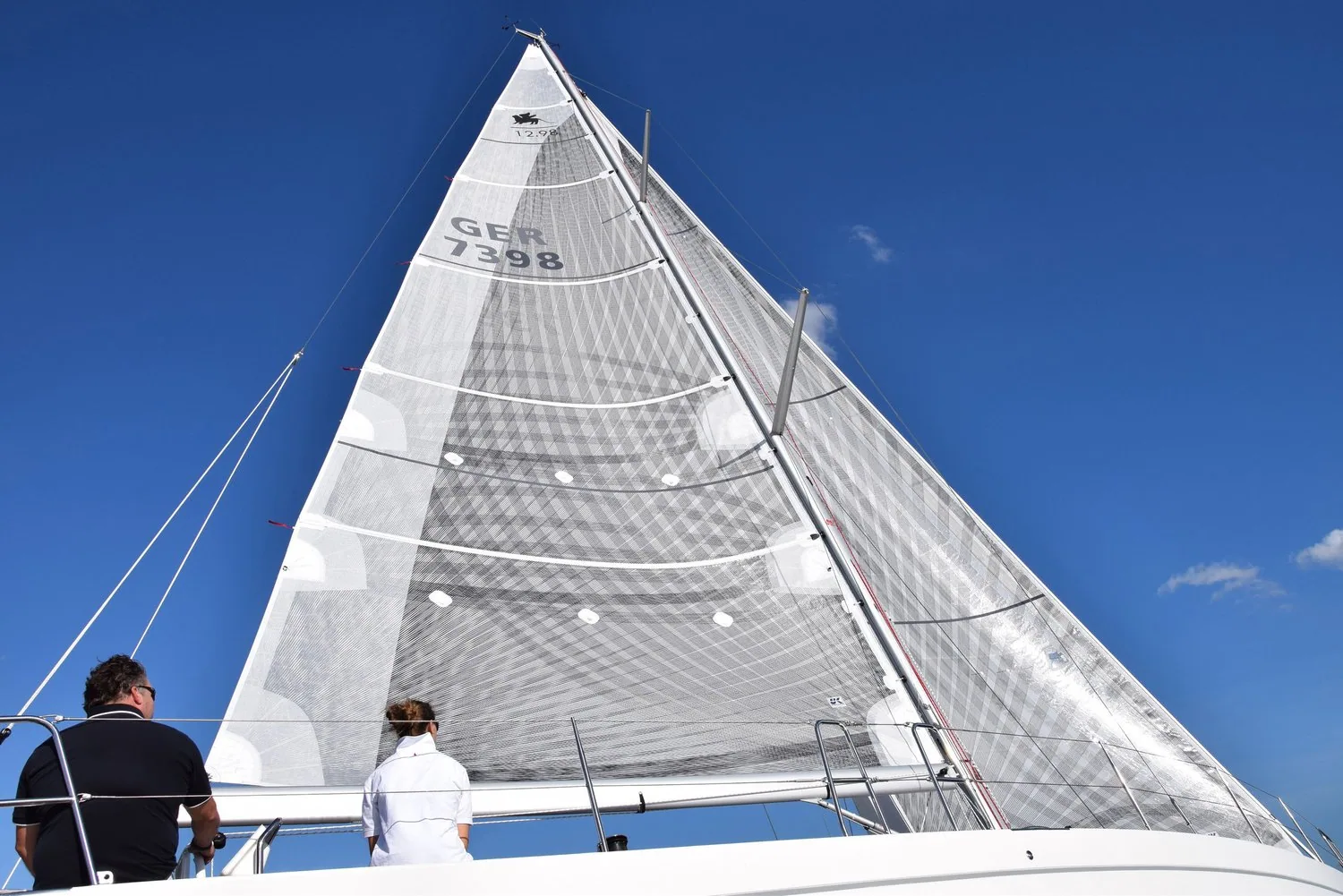 Two sailors on deck below a light grey X-Drive® genoa, sail number GER 7398, tape grid showing against a blue sky