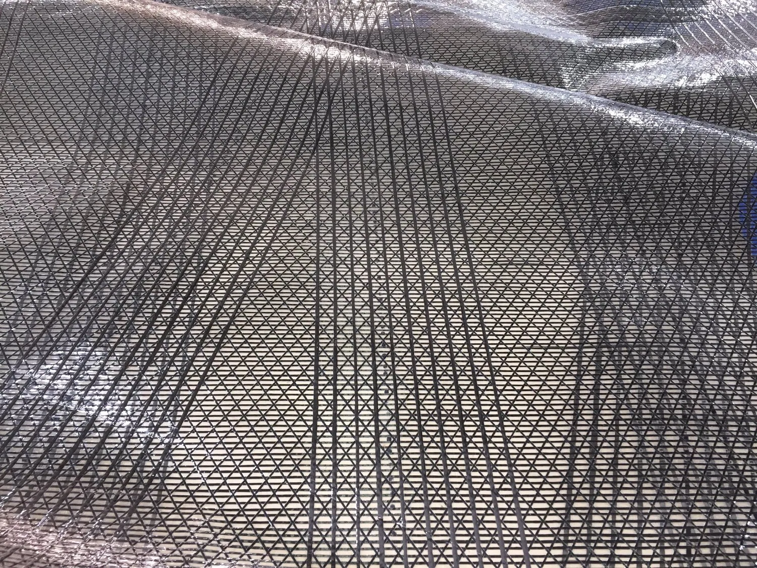 Close-up of X-Drive® carbon sailcloth: dense black carbon tapes crossing over a silver laminate