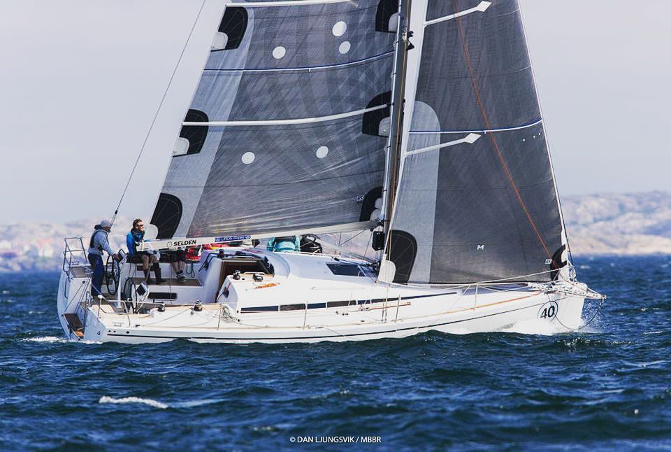 White 40-foot racer-cruiser beating upwind under grey X-Drive® mainsail and genoa, two crew aboard, rocky islands behind