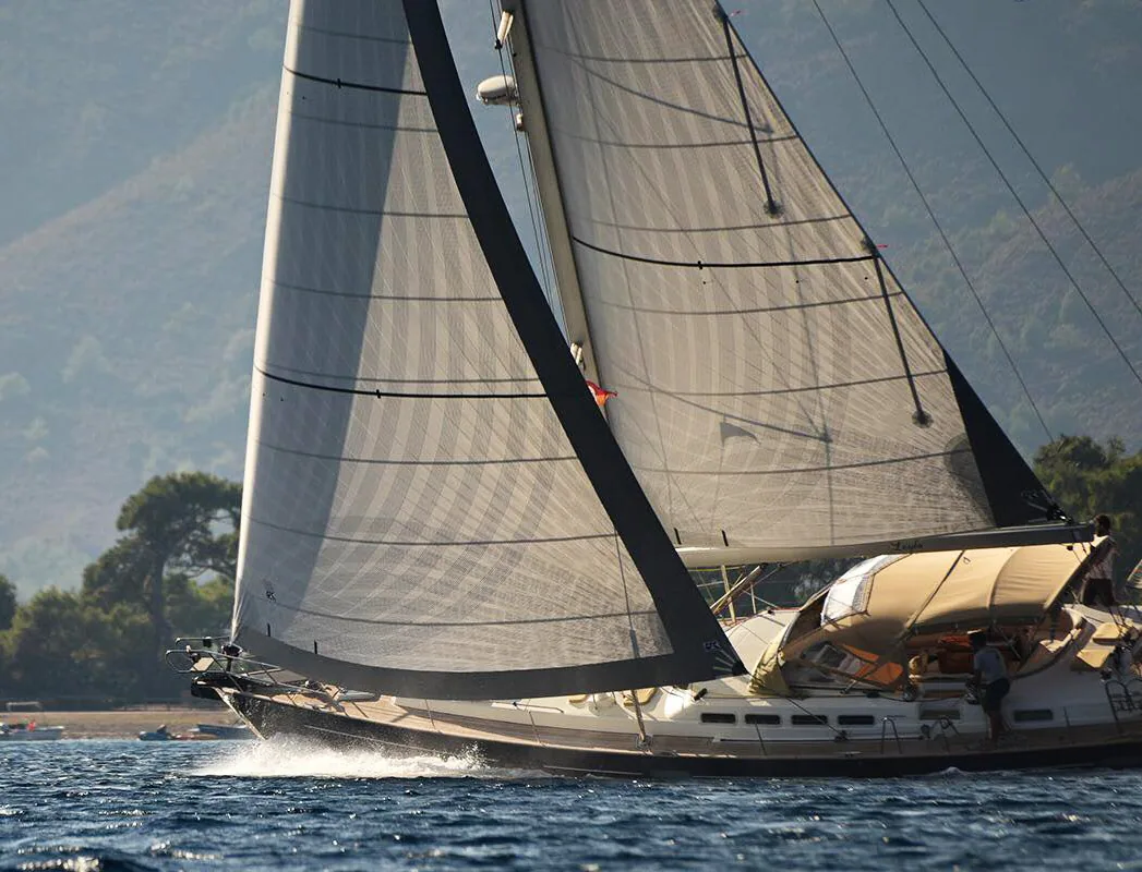 Large cream-hulled cruising yacht sailing past wooded hills under grey X-Drive® mainsail and genoa with dark leech tapes