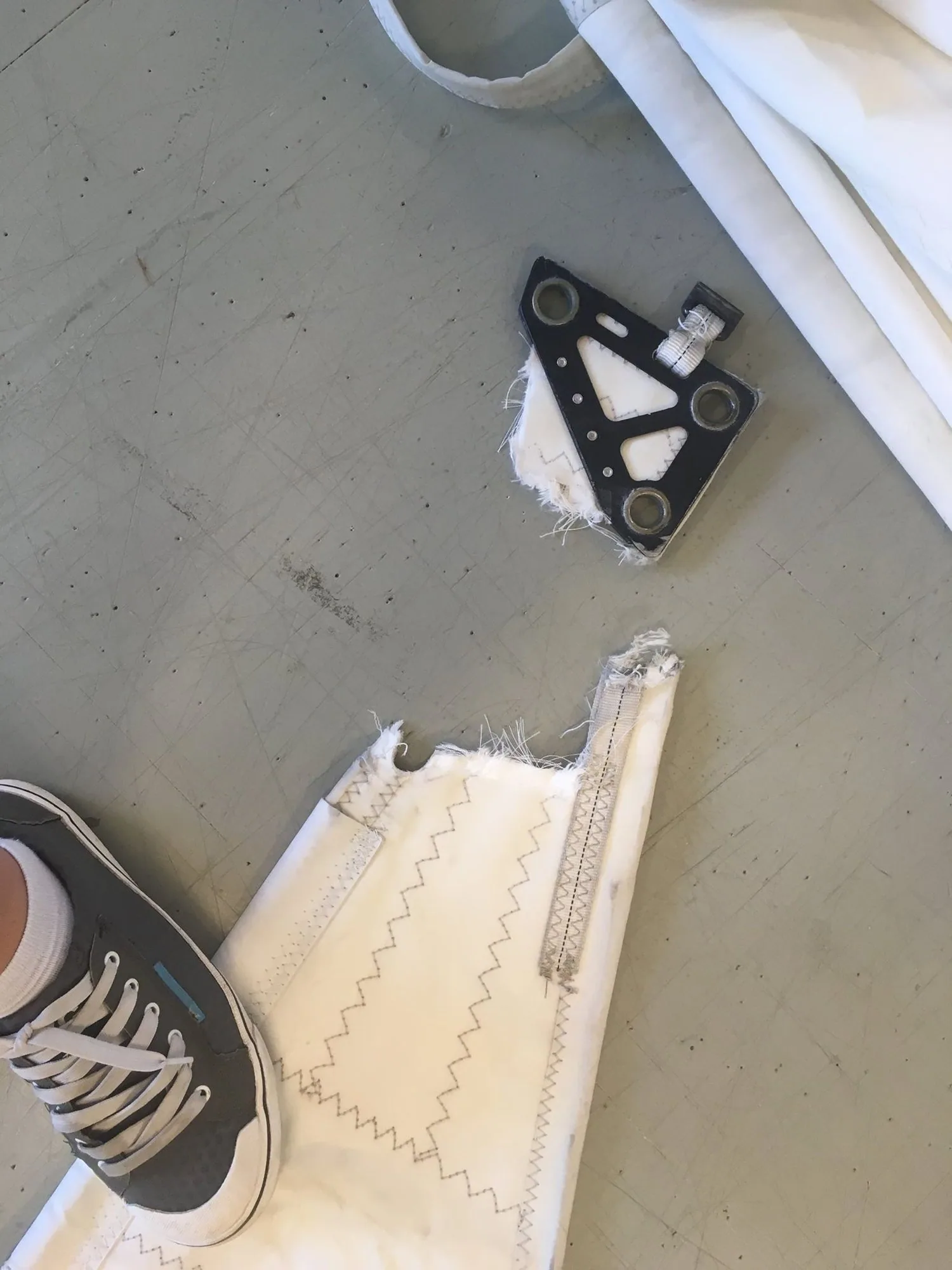 Torn-off black headboard lying on a loft floor beside the ripped head of a white mainsail, a sneaker in the corner