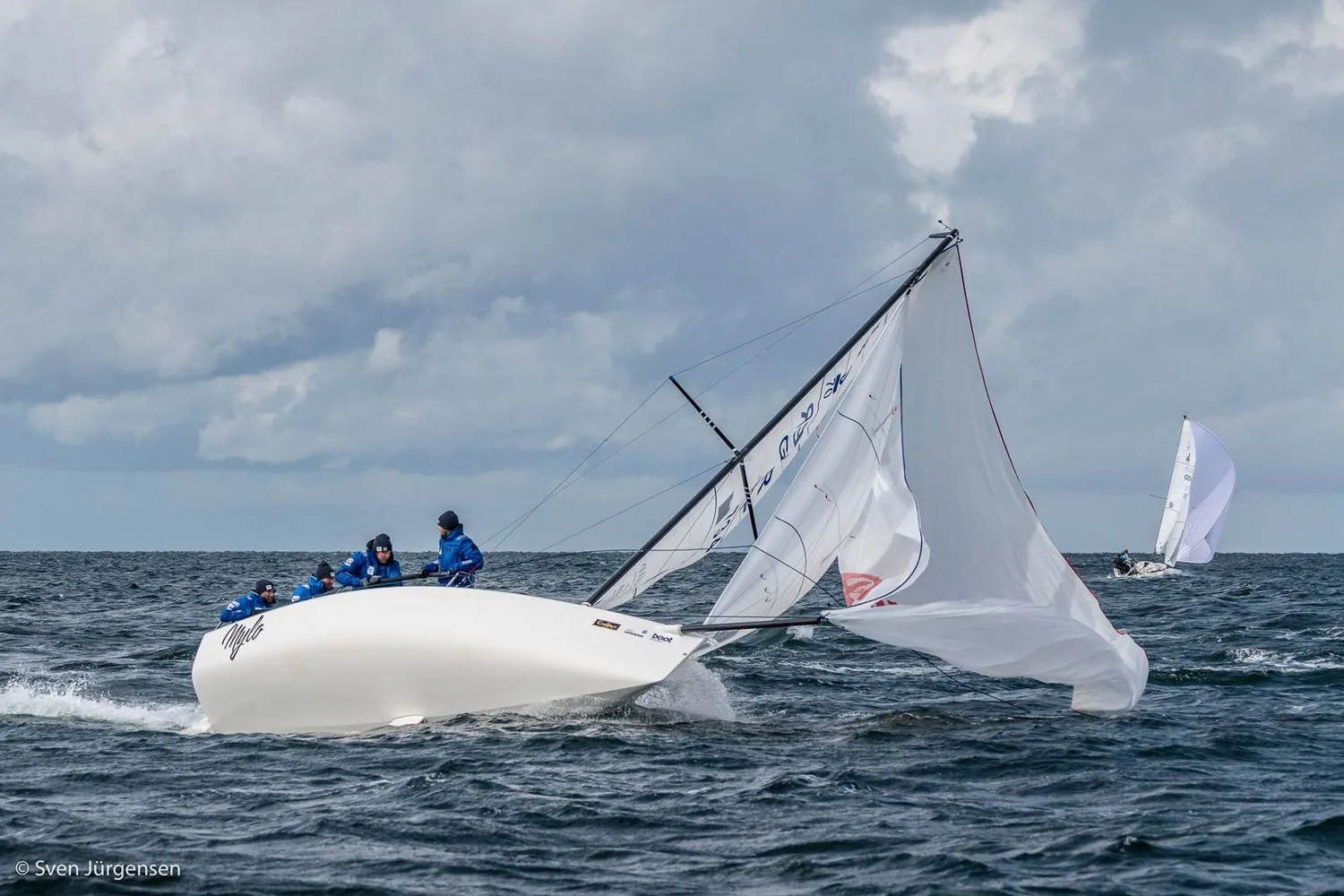 J/70 MYLO broaching downwind, spinnaker collapsed onto the water and crew in blue clinging to the high side