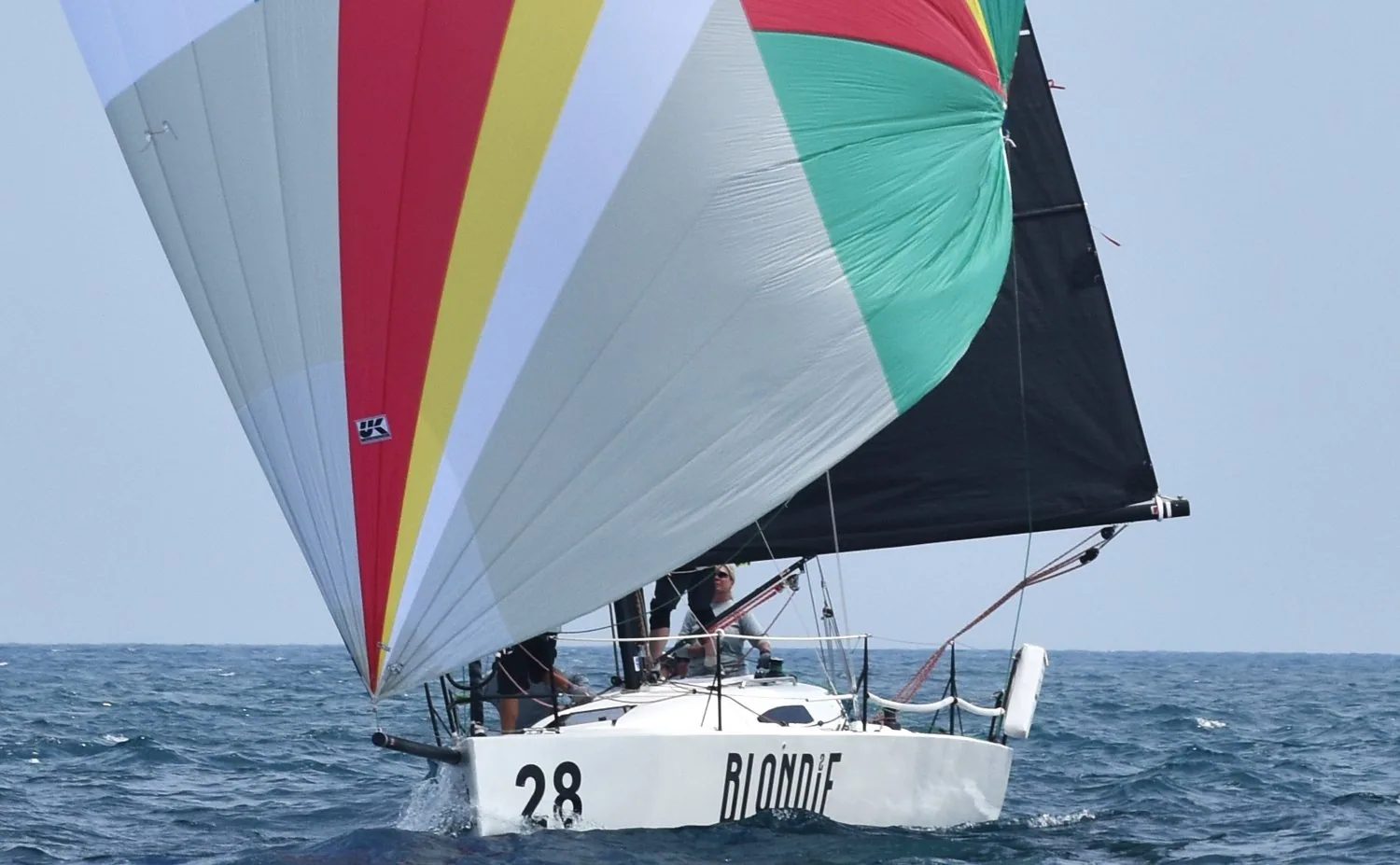 J/88 BLONDIE, number 28, sailing downwind under a red, yellow, white and green asymmetric spinnaker and black mainsail