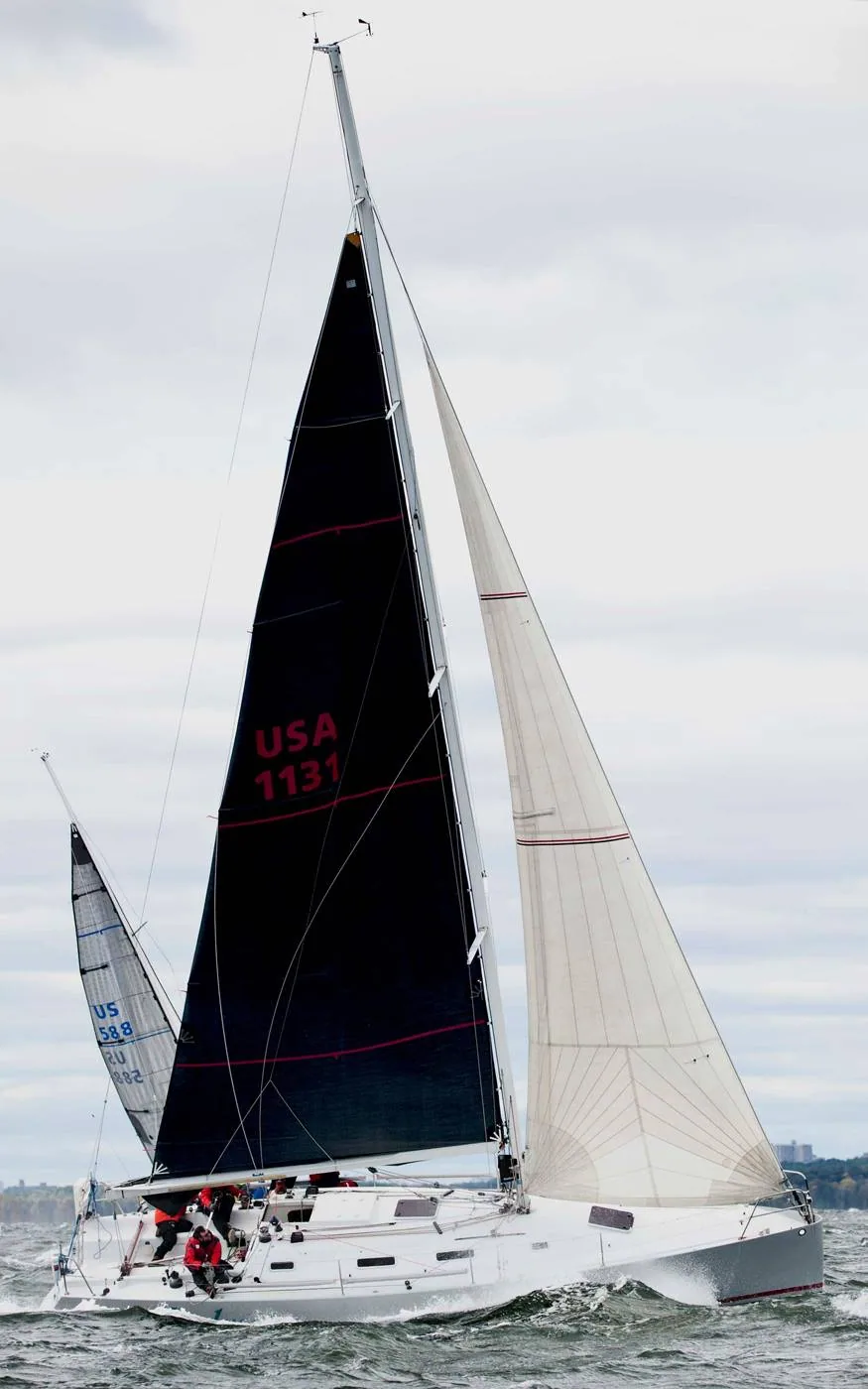 Racer-cruiser USA 1131 beating upwind under a black mainsail and white genoa, crew in red, US 588 astern