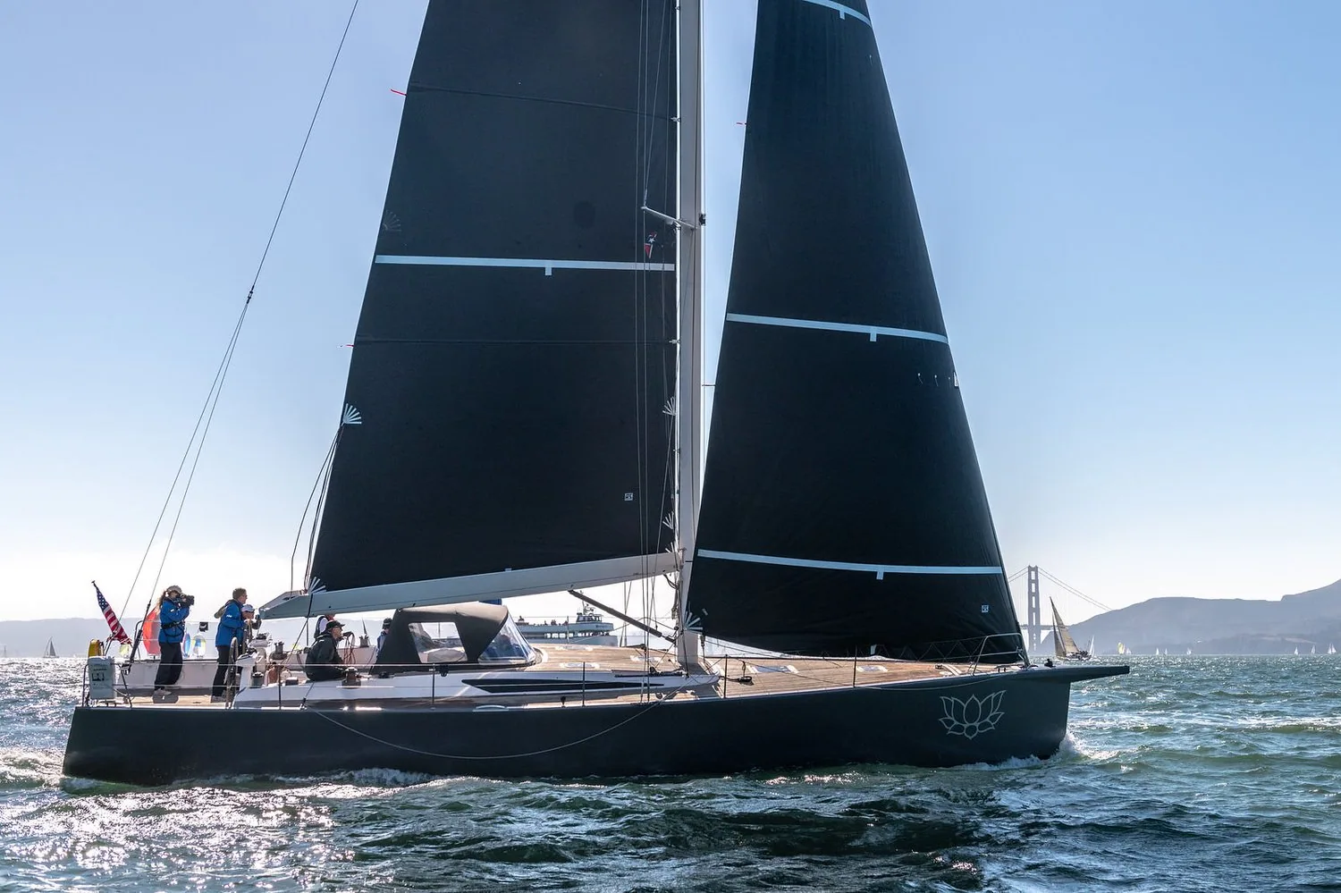 Vismara 50 LOTUS, black hull and black Uni-Titanium Liteskin mainsail and jib, crew aft, red suspension bridge on the horizon