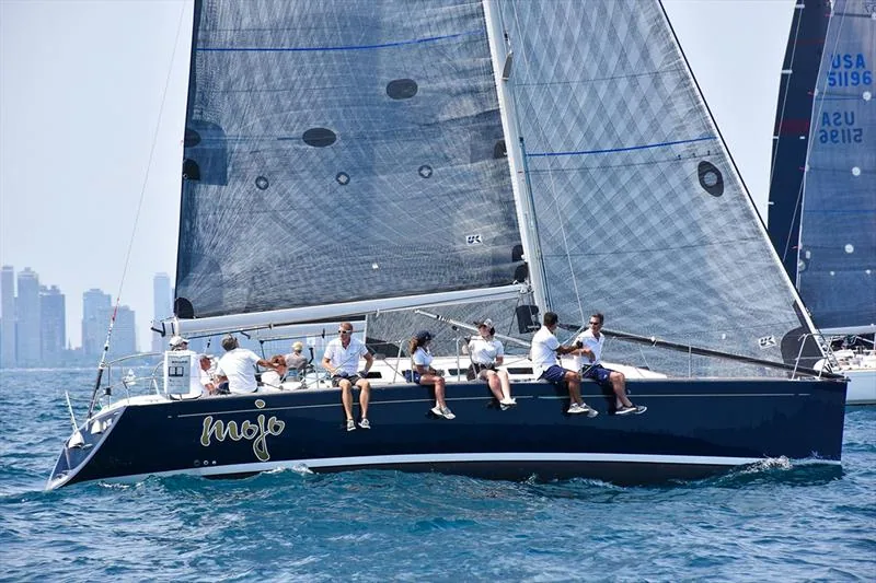 Beneteau First 40.7 MOJO, dark blue hull, seven crew on the rail, grey laminate sails, Chicago skyline hazy behind