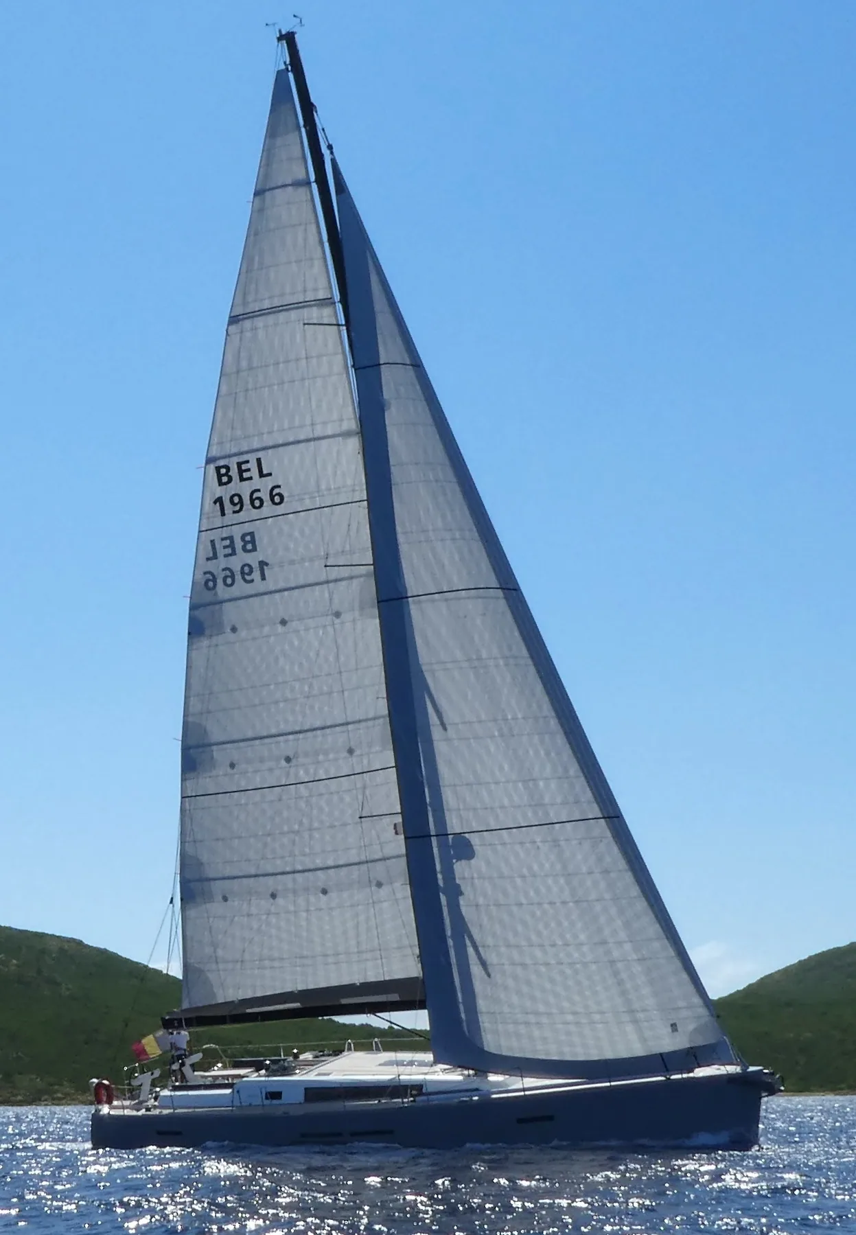 Centurion 57 under grey laminate mainsail and genoa, sail number BEL 1966, sailing past green hills