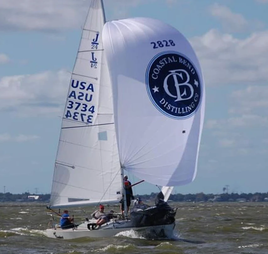 J/24 MISS CONDUCT, USA 3734, running under a white spinnaker with a Coastal Bend Distilling Co. logo, crew of five