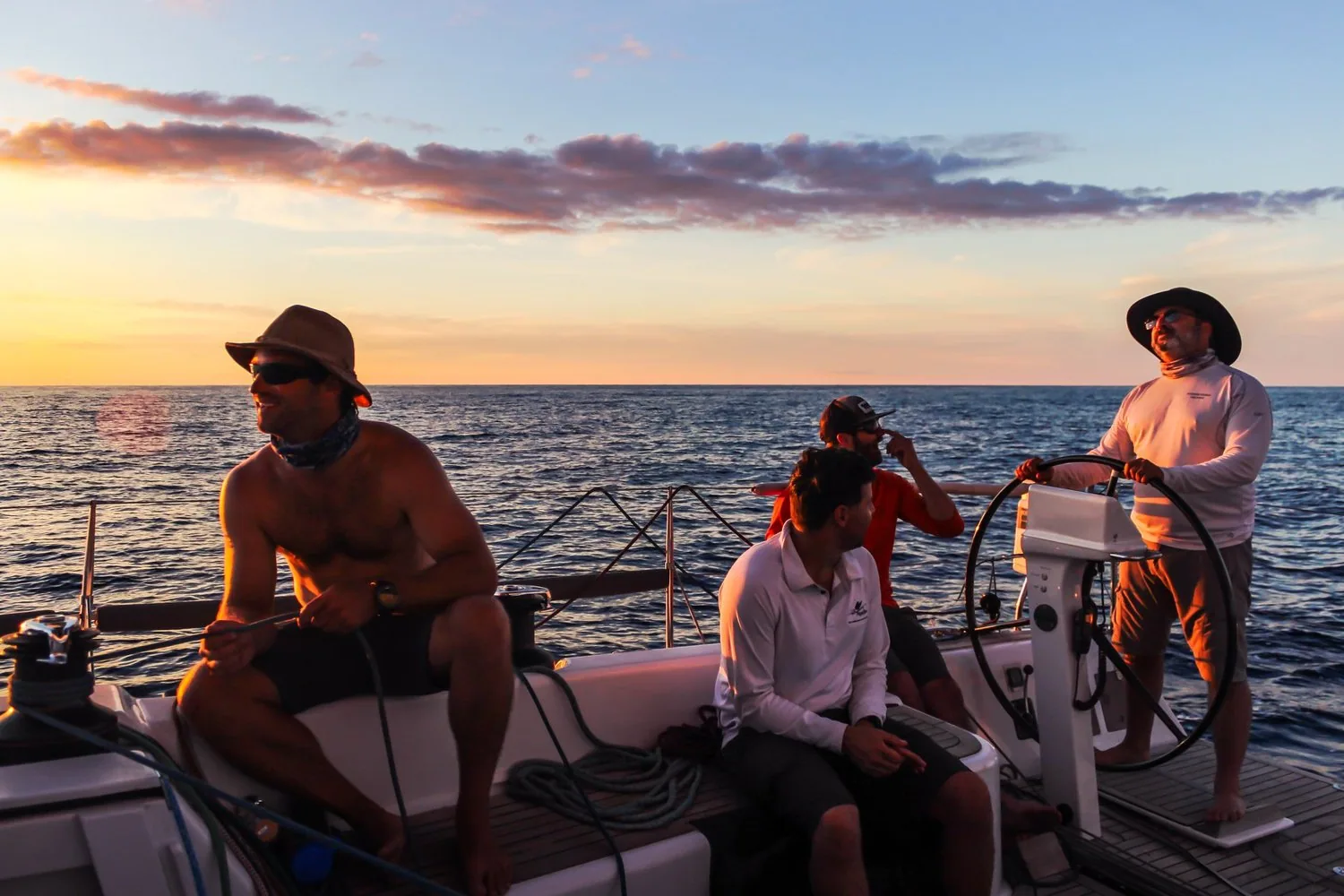 Four crew of SUMMER STORM on deck at sunset in light air, the helmsman standing at the wheel, 2018 Newport Bermuda Race