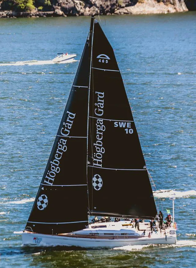 Arcona 465 FLYT under black Uni-Titanium sails with Högberga Gård lettering, sail number SWE 10, among rocky islands