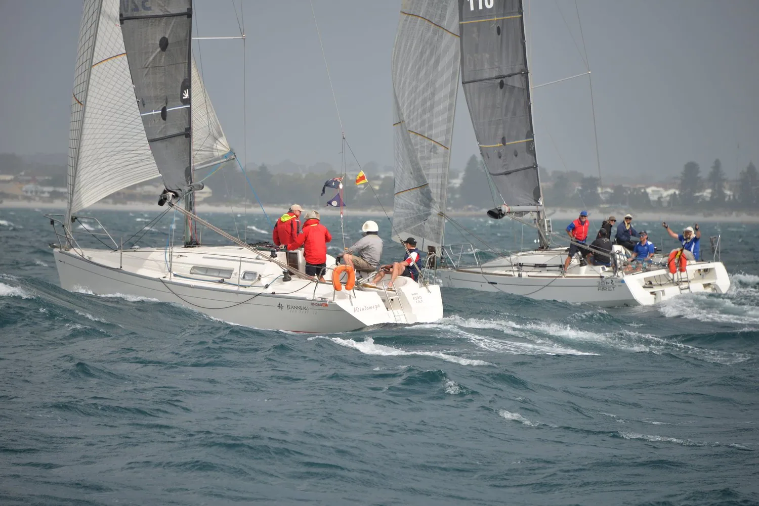 Two Sun Fast 32s racing side by side in a grey chop, crews in red on deck, low coastline behind