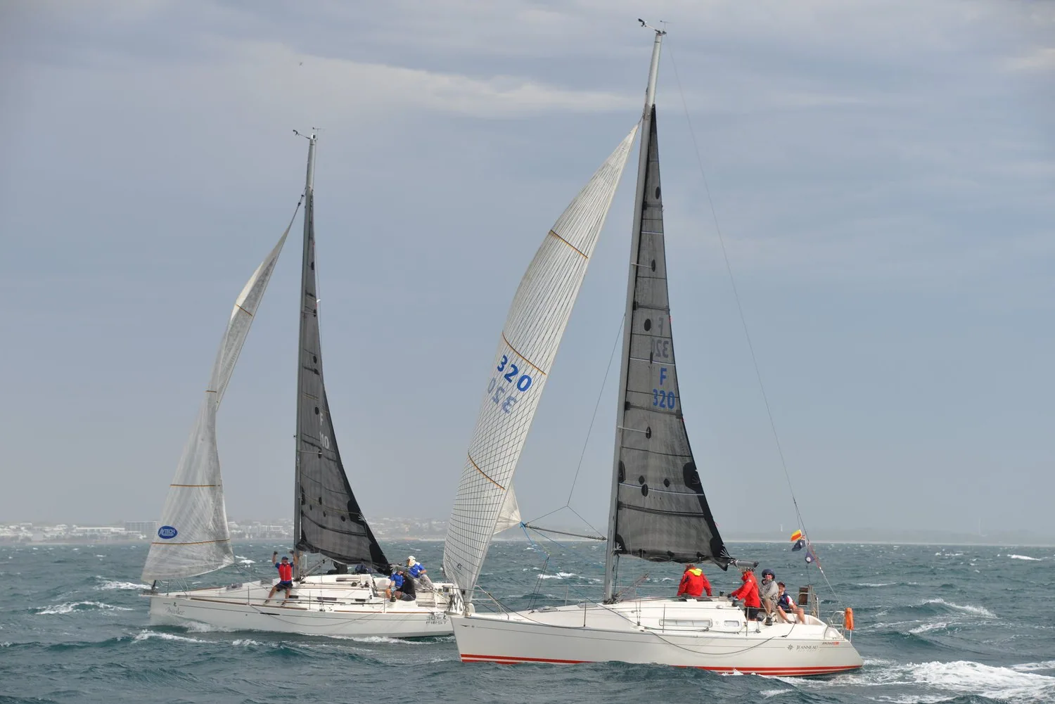 Two Sun Fast 32s beating upwind in a grey chop, the nearer boat with a white genoa numbered 320, crews on the rail