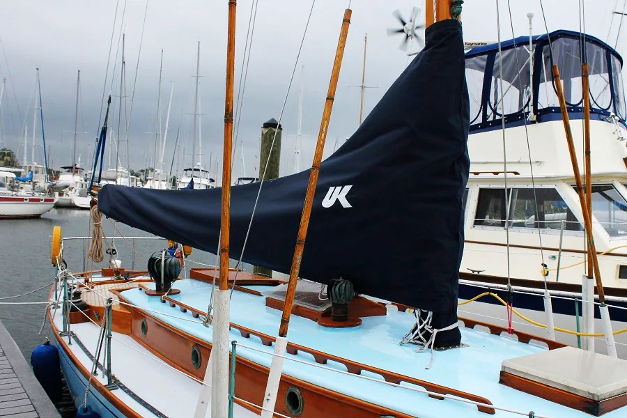 Navy blue UK Sailmakers mainsail cover on the wooden boom of a classic yacht with a pale blue deck in a marina