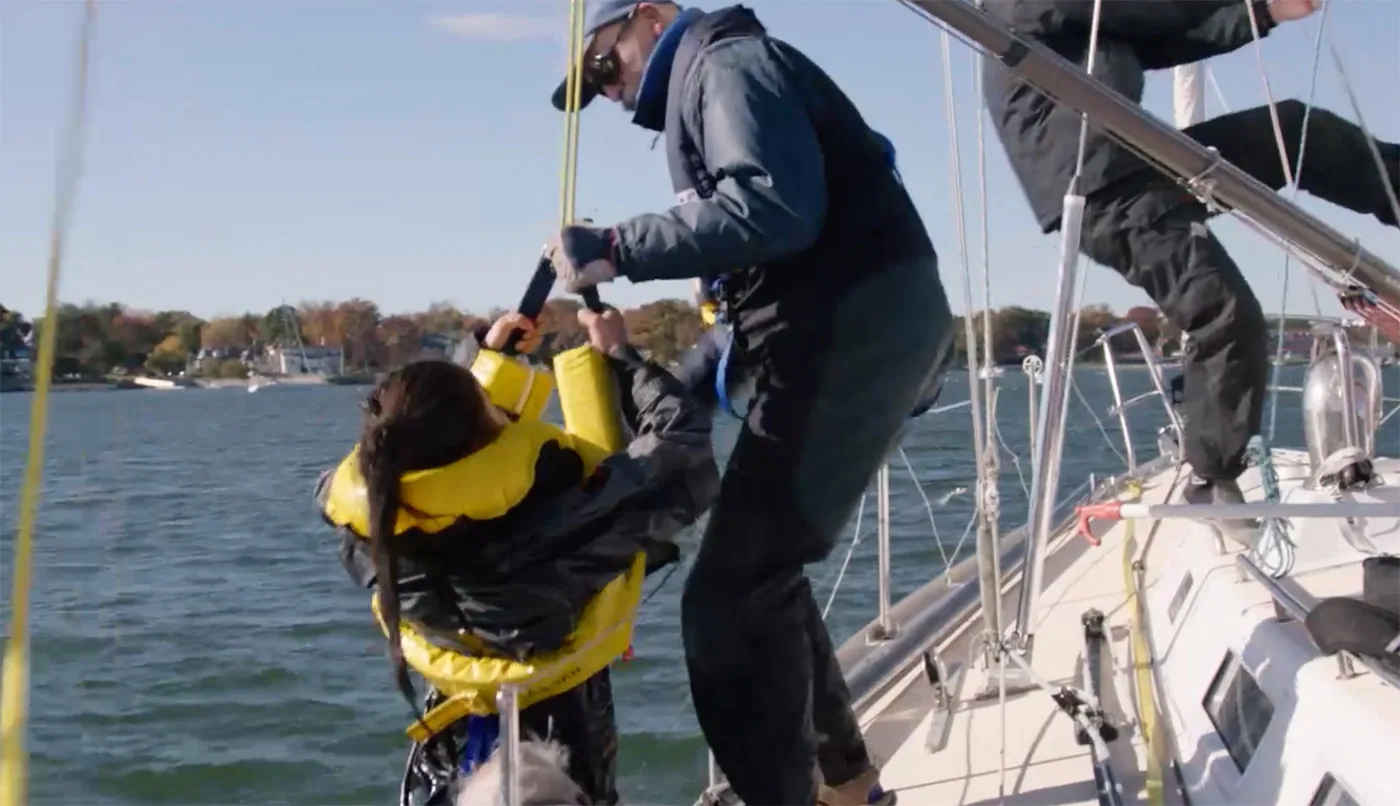 Two crew hauling a person in a yellow life jacket back aboard over the rail during a Lifesling recovery drill
