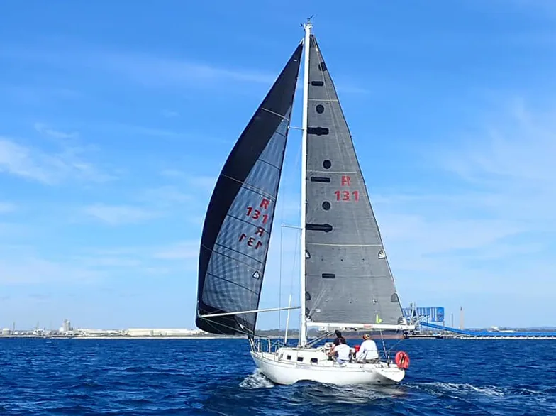 HUCKLEBERRY running wing-on-wing under a dark grey laminate mainsail and poled-out genoa, sail number R 131, port behind
