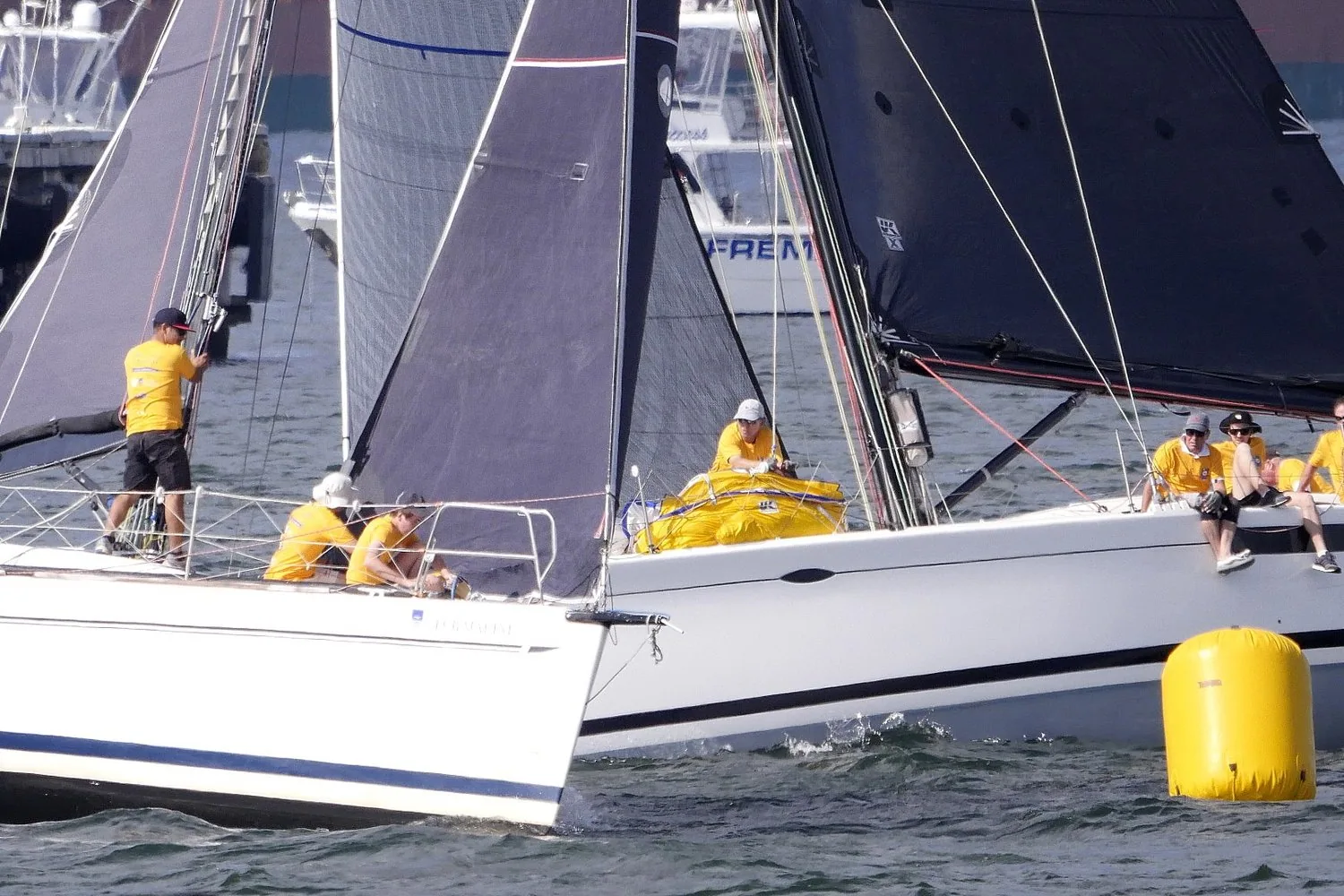Two racing yachts with yellow-shirted crews converging bow to bow at a yellow inflatable mark